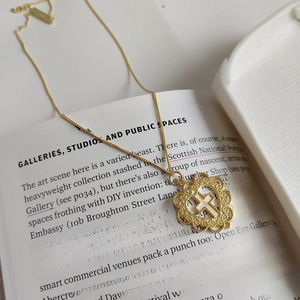Golden 925 sterling silver necklace with cross and heart pendant on a stylish art book
