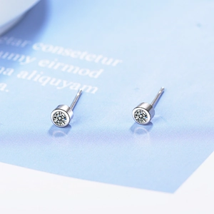 Minimalist silver leaf stud earrings with white zircon stones on a light blue background
