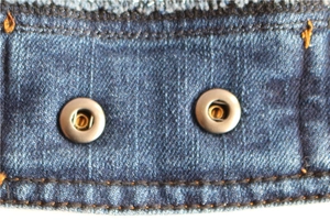 Detail of vintage denim pet vest showing dark blue fabric texture and metal buttons