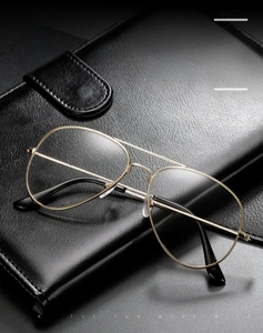 Close-up of golden aviator metal frame glasses on black leather notebook texture
