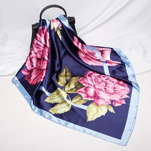 Detail of silk-like scarf with large pink rose print draped over a dark handbag