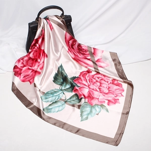 Detail view of a luxury silk-like scarf featuring red rose patterns on a light beige base