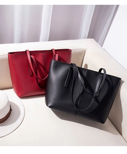 Minimalist red and black tote bags displayed on a white sofa with a stylish straw hat