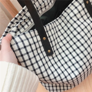 Detail of checkered tote bag with leather strap, zipper closure and rivet accents