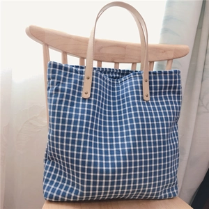 Detail of leather handles and bronze rivets on the blue checkered cotton tote bag