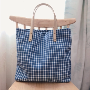 Blue and white checkered canvas tote bag with leather handles on a wooden chair