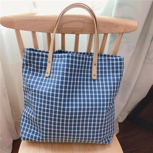Detailed view of plaid cotton tote with leather handles and metal rivets on a wooden chair