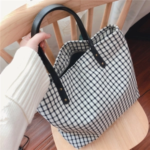 Detail of checkered cotton tote bag showing black leather handles and metal rivets