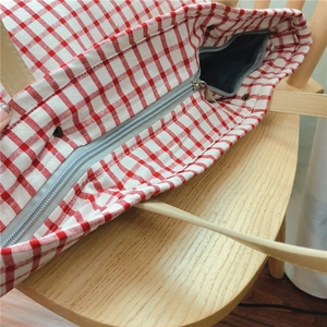Close-up of red plaid cotton tote bag featuring metal zipper and leather handle details