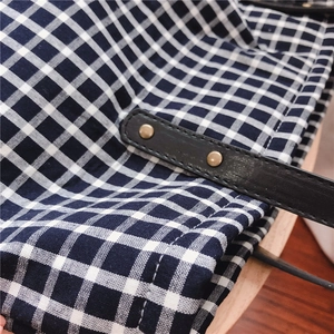 Detail of gingham cotton tote bag featuring black leather strap and golden metal rivets