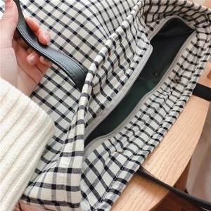 Detail view of black and white plaid canvas tote with leather handle and zipper closure