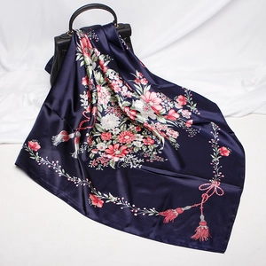 Detail of silk-like blue floral square scarf draped on a black leather handbag