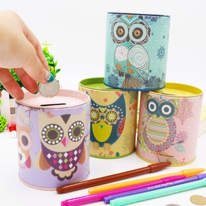 Close-up of a hand inserting a coin into a cute owl pattern metal piggy bank