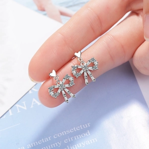 Elegant silver bow earrings with sparkling zircons held to show compact size