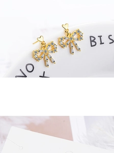 Close-up of golden bow-shaped stud earrings with sparkling cubic zirconia and heart details