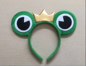 Detail of green plush frog headband with gold crown on light wood background