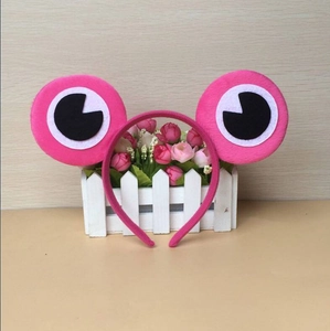 Pink plush frog headband with large cartoon eyes on a decorative white fence