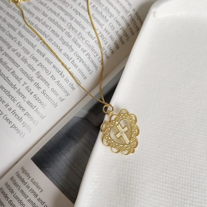 Detail of gold heart pendant with hollow lace design and central cross motif