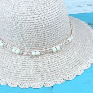 Pink woven straw sun hat with wavy brim and pearl bead band on blue wood background