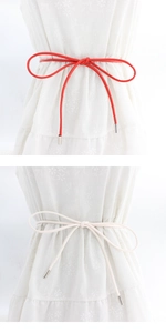 Detail of red and cream waist ropes with silver metal tips on a floral dress