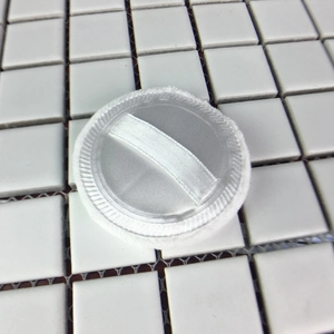 Top view of a soft white round cotton powder puff with a satin ribbon on a tile grid