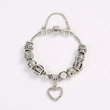 Detailed view of silver snake chain bracelet featuring a sparkling heart charm and safety chain