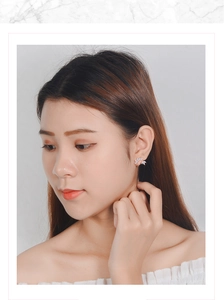 Detailed close-up of a silver leaf-shaped stud earring with zircon stones on a model ear