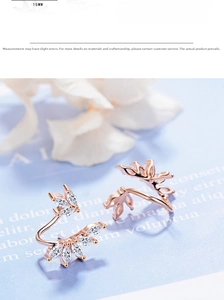 Detail of rose gold flower leaf ear clips with zircon stones on a blue background