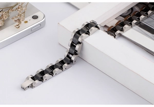 Close-up of matte silver and black ceramic link bracelet on a white wooden frame