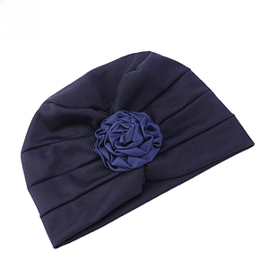 Détail d'un turban plissé bleu marine avec une décoration de rose en tissu superposé