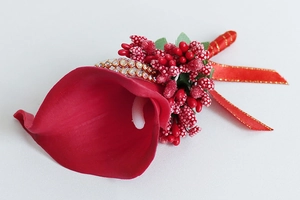 Detail of a red calla lily wedding boutonniere with gold-edged ribbon and red berries