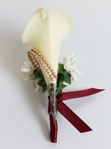 Detail of white calla lily boutonniere with dark red ribbon and gold rhinestone ring