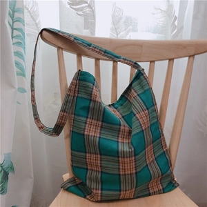 Détail du sac cabas en toile à carreaux vert et orange accroché à une chaise en bois