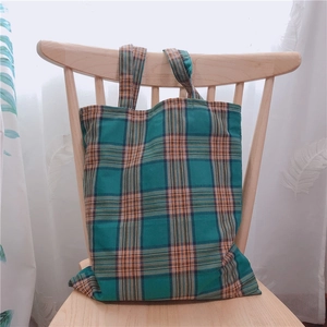 Détail d'un sac cabas en toile à carreaux vert et orange suspendu à une chaise