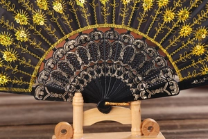 Close-up of black folding fan with gold embroidery, sequins and carved bamboo ribs