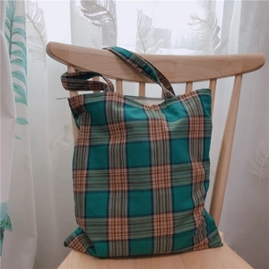 Détail d'un sac cabas rétro en toile à carreaux vert et orange sur une chaise