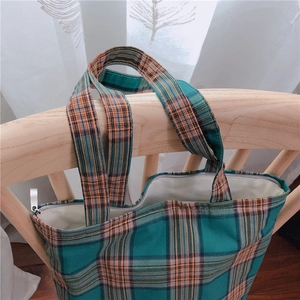 Détail du sac cabas à carreaux vert et orange avec fermeture éclair suspendu à une chaise