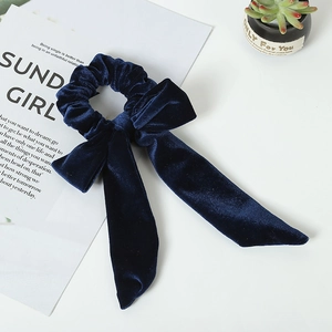 Detail of dark blue velvet bow scrunchie with long ribbon tails on white desk