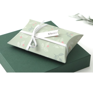 Detail of small green floral pillow gift box with white ribbon and Merci tag label