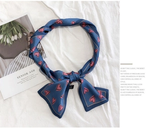 Detailed view of a blue silk scarf with pink heart patterns tied in a stylish bow knot