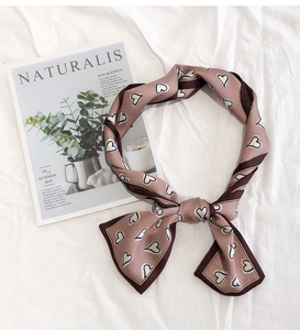 Pink and brown heart pattern silk scarf tied in a bow on a white fabric background