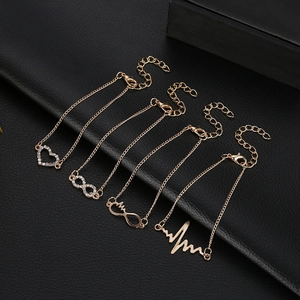 Detail of four-piece gold bracelet set with heart and infinity charms on black leather
