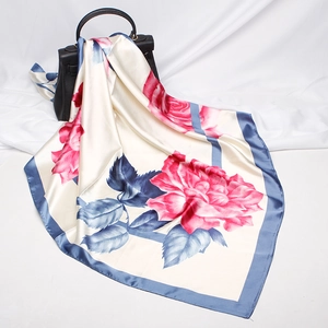 Detail of silk-like square scarf with pink roses and blue border draped on handbag