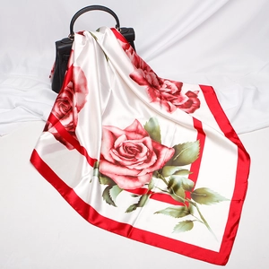 Detailed view of white silk scarf with large red rose print and decorative handbag