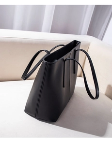 Detail of a large black matte tote bag with long handles placed on a white leather sofa