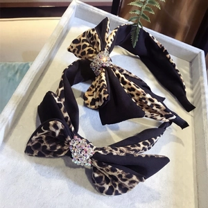 Pair of leopard print bow headbands with rhinestones on a gray velvet jewelry display