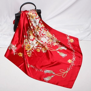 Detail of red floral silk scarf with tassels draped over a black luxury handbag