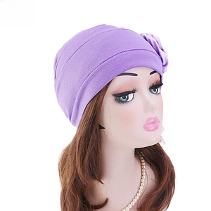 Détail du turban plissé violet avec une grande fleur décorative en tissu sur le côté