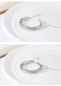Detailed view of silver feather textured open rings on a white decorative ceramic tray