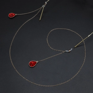 Golden eyewear chain with red teardrop pendants on a black textured background